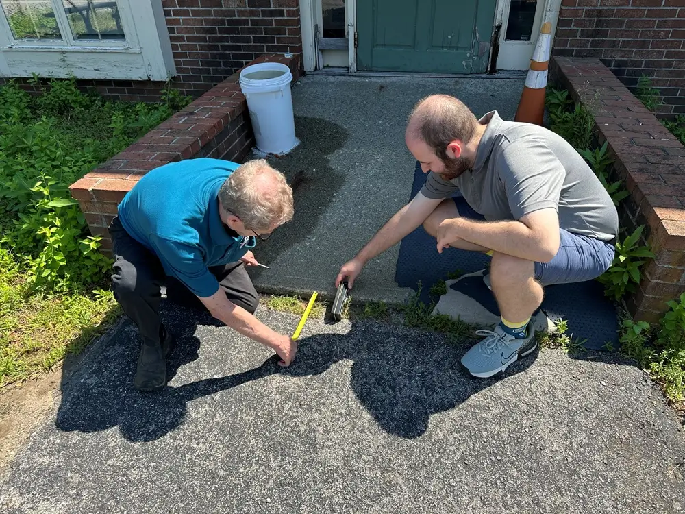 Jim Lyons and Brandon measuring the slope and transition at a building entrance.