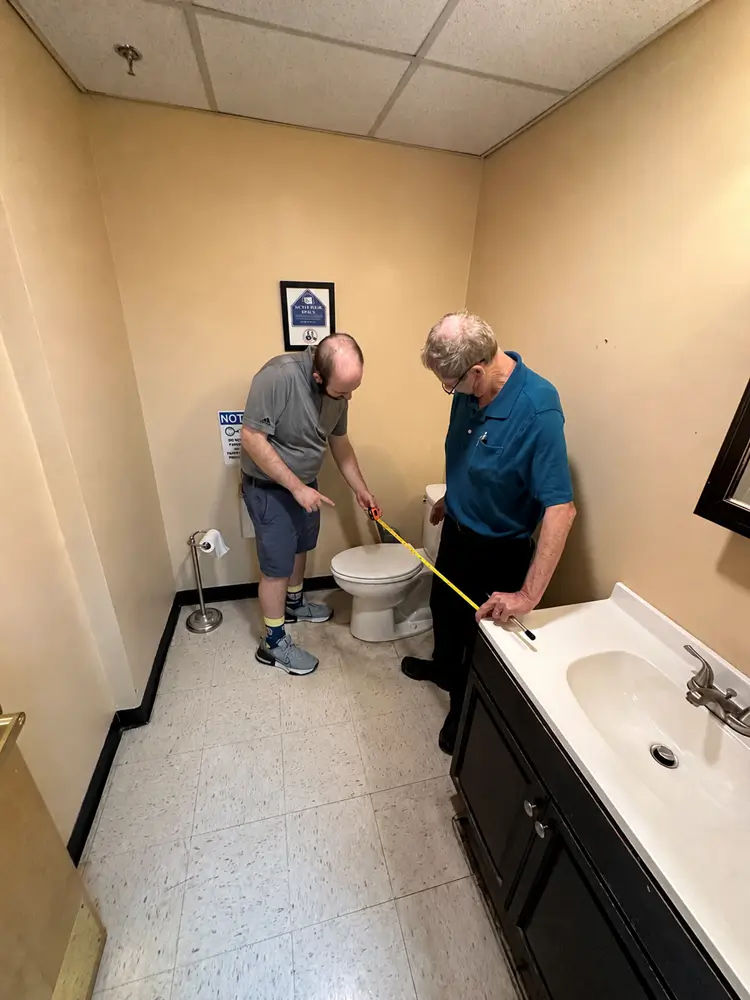 Jim Lyons and Brandon measuring clear space in a restroom during an accessibility review.